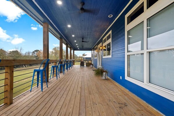 A covered outdoor deck with wooden flooring, blue walls, and a row of blue chairs.