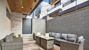 Un patio moderno al aire libre con mobiliario de mimbre, un brasero y vistas a un edificio de fachada de piedra.