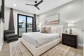 A bedroom with a bed, a nightstand, a chair, a ceiling fan, a window, and a painting on the wall.