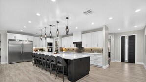 Una cocina moderna con una isla grande, electrodomésticos de acero inoxidable e iluminación colgante.
