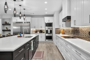 A modern kitchen with white cabinetry, stainless steel appliances, and pendant lighting.