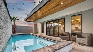 Una piscina con techo de madera, pared de ladrillo y zona de patio con mobiliario de mimbre.