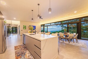 Una cocina moderna con una isla grande, zona de comedor con sillas y vistas amplias a través de grandes ventanales.