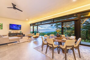 Una sala de estar moderna con comedor, ventanas amplias, ventilador de techo y televisor en la pared.