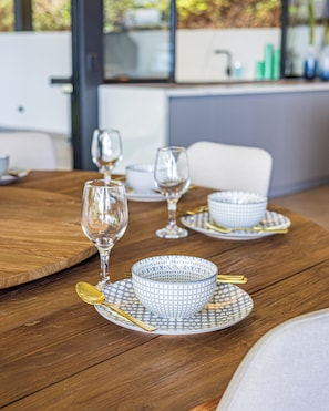 A dining table with a wooden surface, clear glassware, and patterned bowls on placemats. - Brand-New Ocean View Home at a Special Rate (Piedra Amarilla)