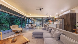 A modern kitchen with dark wood cabinets, a grey sofa, and a dining area with chairs and a table. - Brand-New Ocean View Home at a Special Rate (Piedra Amarilla)