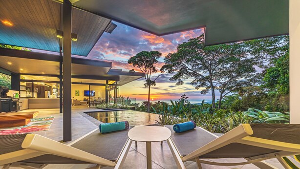 A modern outdoor seating area with a view of the sunset and trees. - Brand-New Ocean View Home at a Special Rate (Piedra Amarilla)