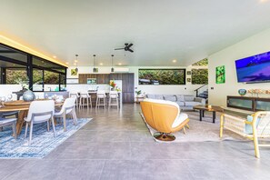 A modern living room with a dining area, a sofa, a TV, and a kitchen in the background. - Brand-New Ocean View Home at a Special Rate (Piedra Amarilla)
