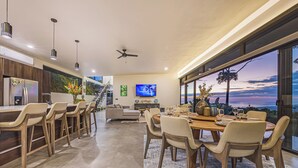 A modern kitchen with a large island, a dining area with a view, and a living space with a TV. - Brand-New Ocean View Home at a Special Rate (Piedra Amarilla)