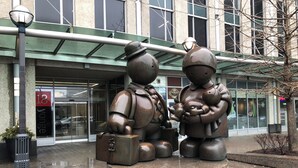 A sculpture of two figures, one holding a suitcase and the other a baby, in front of a building with a glass entrance and a sign reading '18 Yonge.' - 2-bedroom apartment in amazing Toronto with cool AC breeze (Toronto)