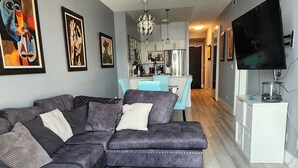 A living room with a sectional sofa, a flat-screen TV, and artwork on the walls. - 2-bedroom apartment in amazing Toronto with cool AC breeze (Toronto)