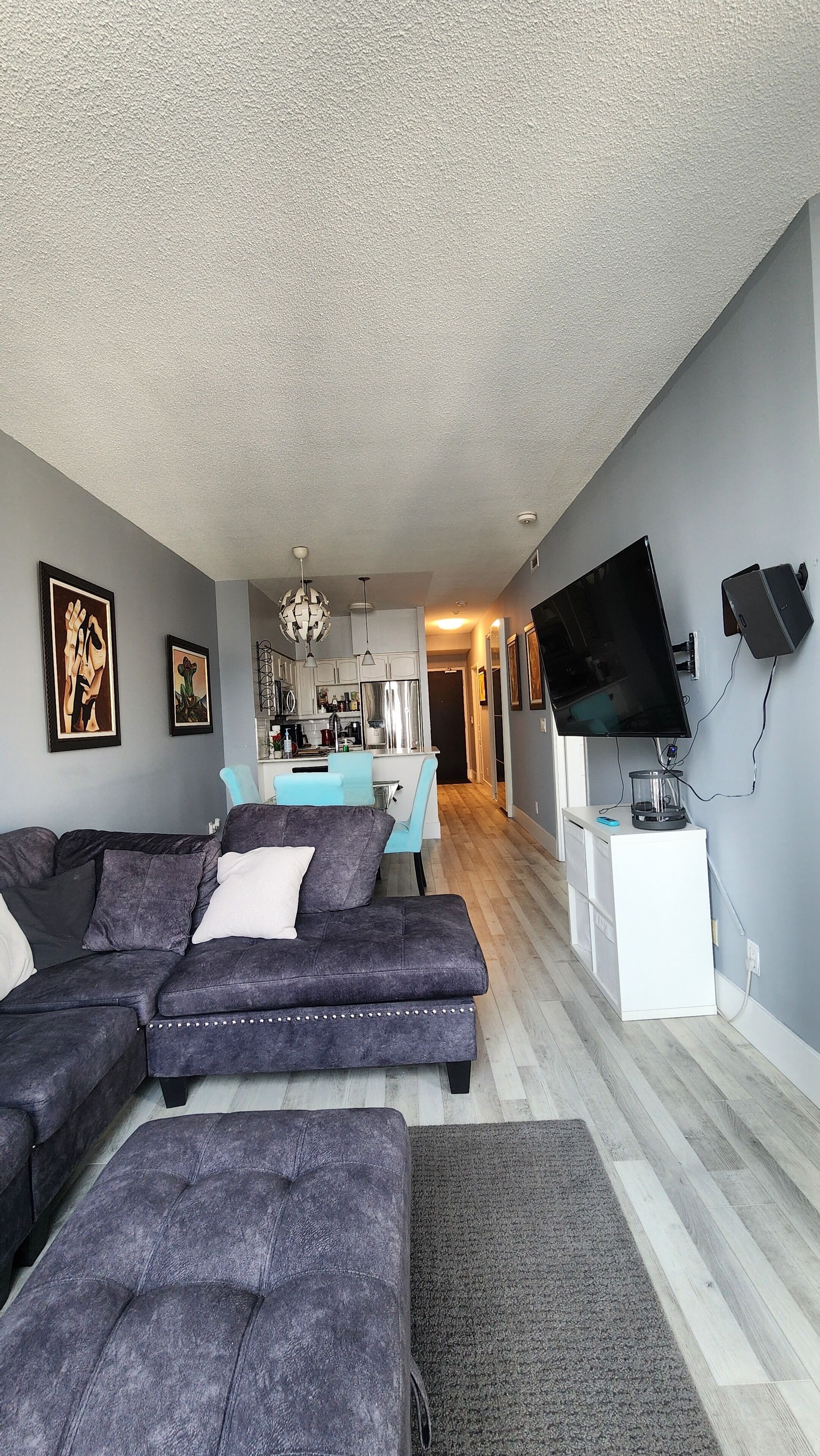 Un salon moderne avec un canapé d’angle, un téléviseur à écran plat et des œuvres d’art accrochées aux murs.