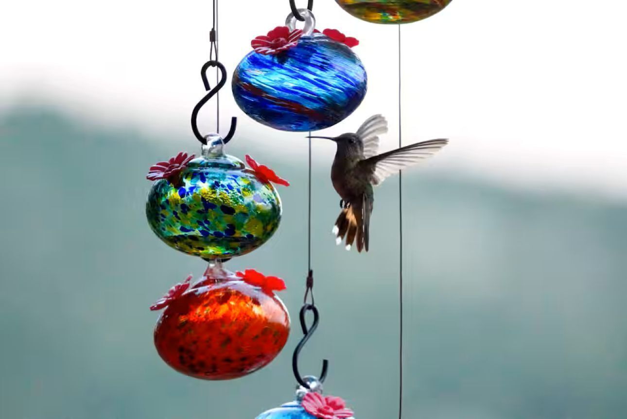A bird feeder with colorful glass balls and red flowers.