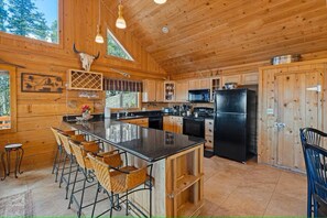 Eine Holzhütte mit einer großen Kücheninsel, Barhocker und einem Kühlschrank.