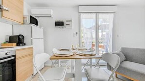 Een moderne keuken met witte apparaten, een eettafel met stoelen en een grijze bank.