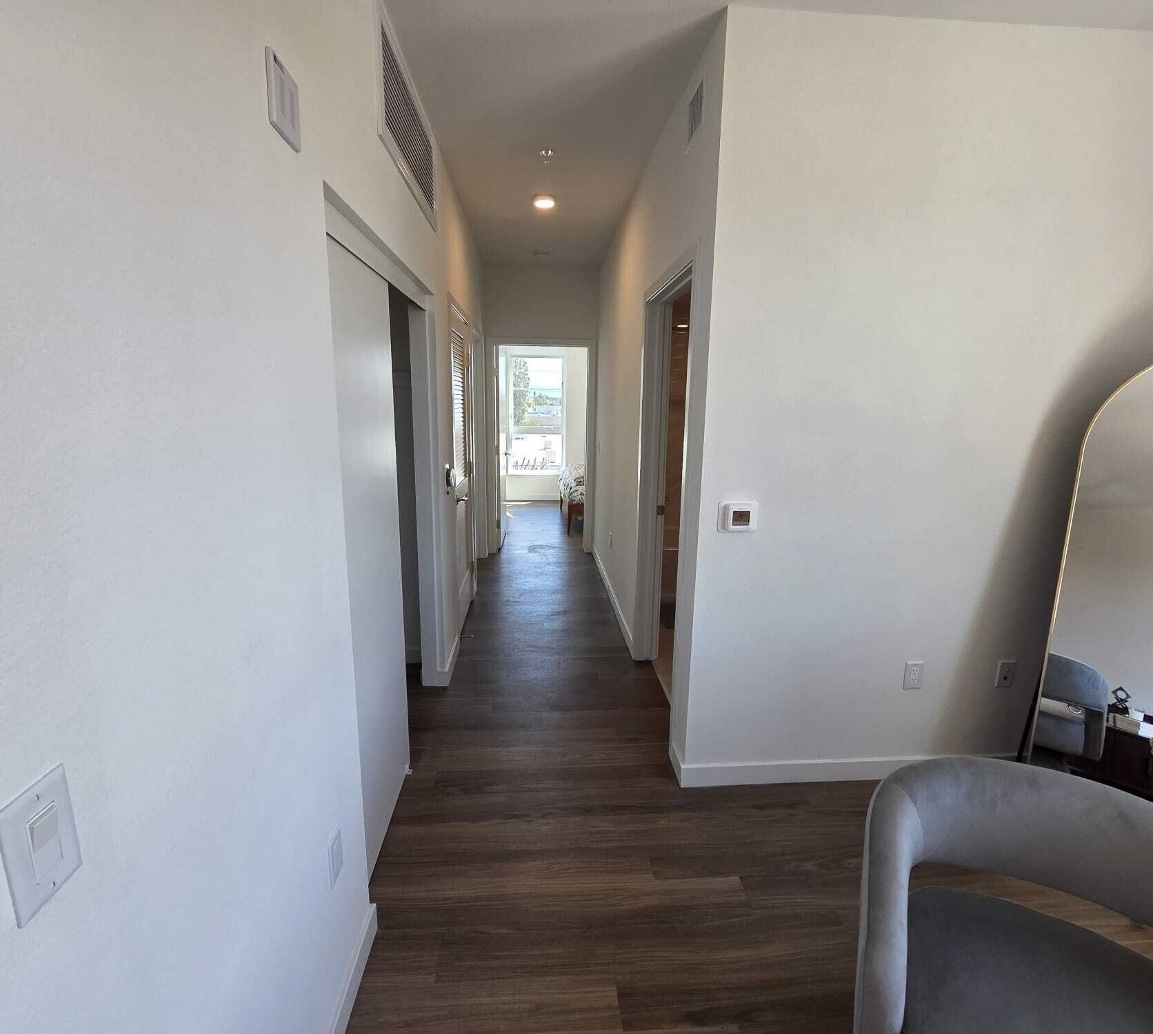 A hallway with wooden flooring, white walls, and doors leading to other rooms.