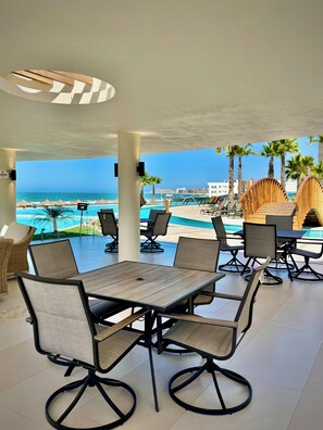 A covered outdoor seating area with tables and chairs, overlooking a pool and beach. - Beachfront Studio at Sonoran Star Resort | Stunning Ocean Views (Puerto Peñasco)