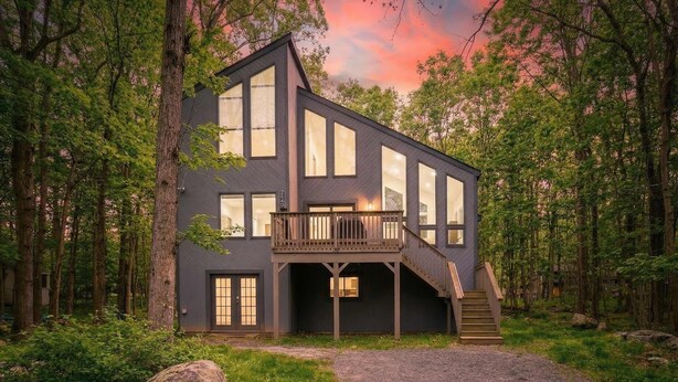 Una casa moderna de dos pisos con balcón, rodeada de un bosque.