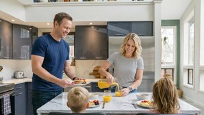 Una cocina moderna con armarios oscuros, encimera de mármol y un comedor con dos adultos y un niño.