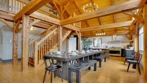 A spacious kitchen with wooden beams, a dining area with a long table, and a staircase. - Pickleball, Sauna, Hot Tub, Cold Plunge, Game Room, Pond, Mini Golf (Broad Top City)