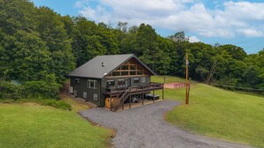 A lodge with a large deck, a covered porch, and a gravel driveway. - Pickleball, Sauna, Hot Tub, Cold Plunge, Game Room, Pond, Mini Golf (Broad Top City)