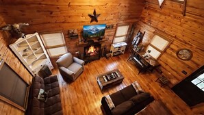 Un acogedor interior de cabaña con chimenea, paredes de madera, un sofá, un sillón y una televisión.