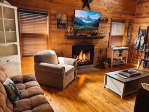 Een gezellig chaletinterieur met een open haard, een televisie erboven en een comfortabele zithoek.