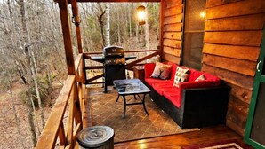 Una terraza de madera con una parrilla, un sofá rojo y una mesita.