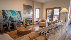 A living room with a sofa, coffee table, TV, fireplace, and a view through a window. - Ski/Bike-In Out | Gondola Steps | Mtn Village Core (Mountain Village)