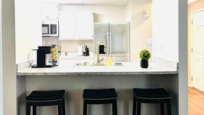 A modern kitchen with a central island, stainless steel appliances, and bar stools. - Hot Tub Oasis Close to Airport 2Bd (Charlotte)