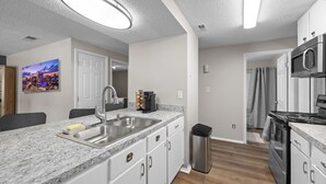 A modern kitchen with granite countertops, stainless steel appliances, and a cityscape painting on the wall. - Hot Tub Oasis Close to Airport 2Bd (Charlotte)