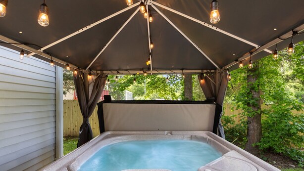 A hot tub under a covered area with a control panel, surrounded by greenery. - Hot Tub Oasis Close to Airport 2Bd (Charlotte)
