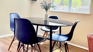 A dining area with a table, chairs, a vase with flowers, a wall sign, and a window with a view of trees. - Hot Tub Oasis Close to Airport 2Bd (Charlotte)