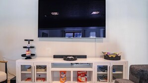 Uma sala de estar com uma televisão de tela plana na parede, um rack branco com prateleiras e um sofá cinza.