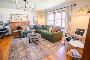 A living room with a sectional sofa, a coffee table, a fireplace, and a bookshelf. - Game Room + Coffee Bar | Near Dining, Parks & Mall (Overland Park)