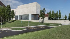 Um edifício moderno com telhado plano, grandes janelas e área de estacionamento com vagas demarcadas.