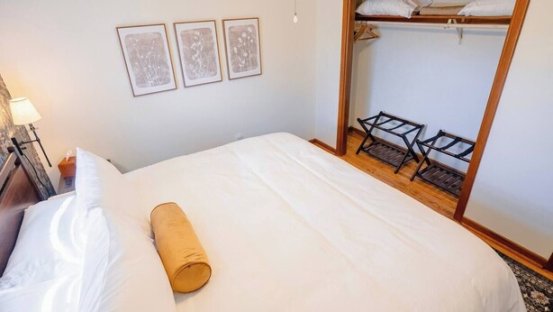 Quarto de hotel com uma cama, um guarda-roupa de madeira e três quadros na parede.
