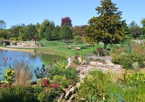 A landscaped garden with a pond, pathways, and benches. - Game Room + Coffee Bar | Near Dining, Parks & Mall (Overland Park)