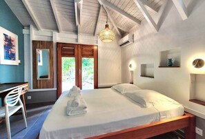 Ein Schlafzimmer mit Bett, Schreibtisch und Stuhl. Eine Tür führt zu einem Außenbereich.