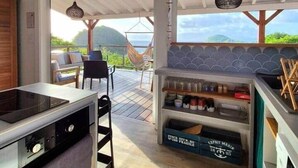 A modern kitchen with a large island, a dining area with outdoor seating, and a view of the ocean. - Villa Bois Coco with a view of Pain de Sucre (Terre-de-Haut)