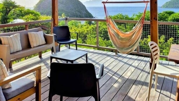 A wooden deck with a hammock, seating, and a view of the ocean. - Villa Bois Coco with a view of Pain de Sucre (Terre-de-Haut)