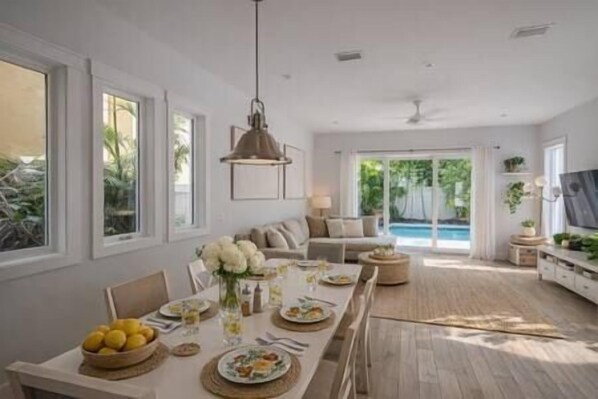 A spacious living area with a dining table set for a meal, a sofa, and a view of a swimming pool.