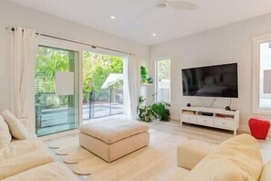 A modern living room with a flat-screen TV, a sofa, and a sliding glass door leading to an outdoor area.