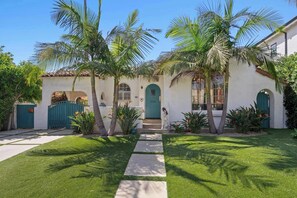 Una casa con facciata bianca, porta verde e palme nel giardino.