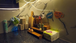 Un plan de travail de cuisine avec des boîtes étiquetées « THÉ », « SUCRE » et « CAFÉ », une planche à découper en bois, un bloc à couteaux et une tasse sur laquelle est inscrit « Le café me rend heureux ».