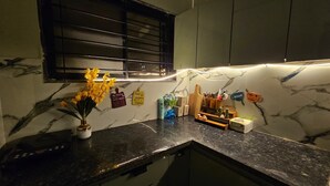 Une cuisine dotée de plans de travail en marbre, d’une fenêtre avec des stores et de divers ustensiles et appareils de cuisine.