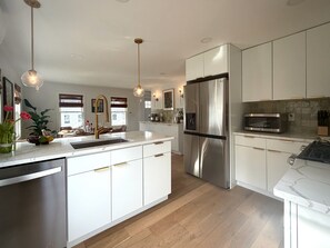 A modern kitchen with white cabinetry, stainless steel appliances, and pendant lighting.