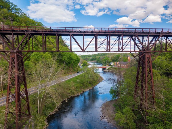 A steel bridge over a river with a road on either side, surrounded by greenery and a clear sky. - Trail-front Hudson Valley Retreat in Rosendale (Rosendale)