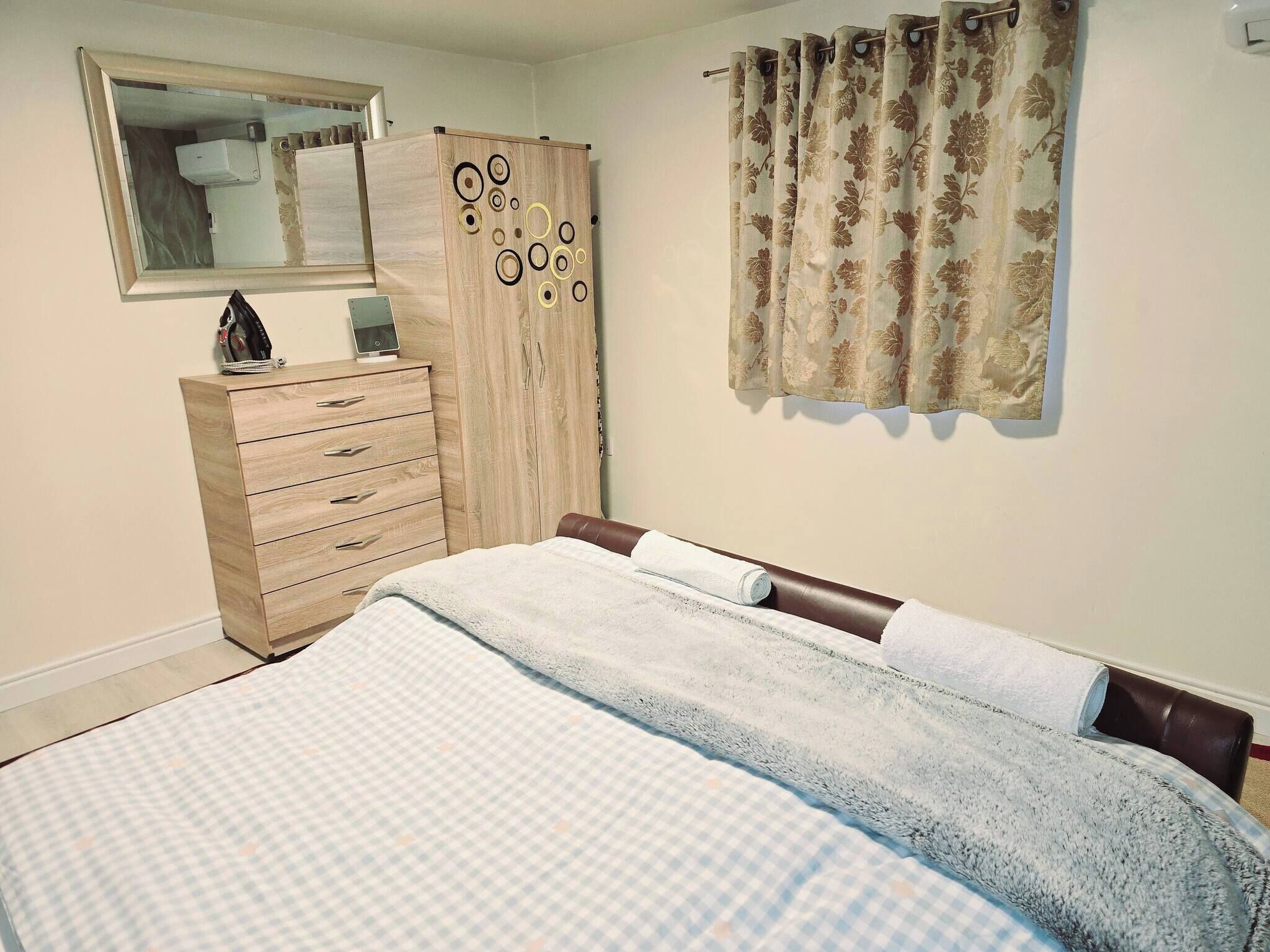 A bedroom with a bed, a wooden wardrobe, a mirror, and a window with curtains.