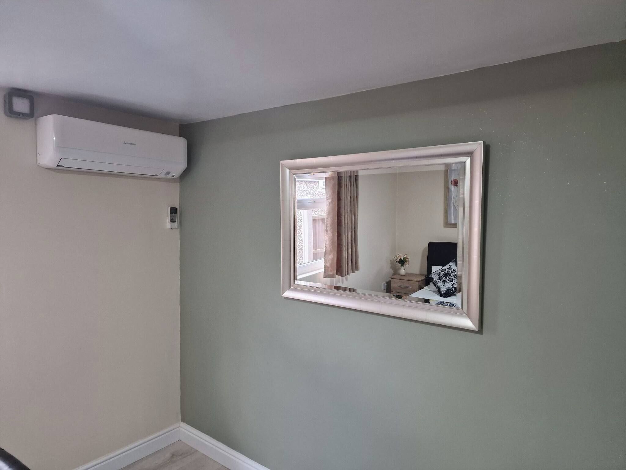 Une pièce dotée d’un grand miroir, d’un climatiseur fixé au mur et d’une petite table de chevet sur laquelle se trouve un vase.